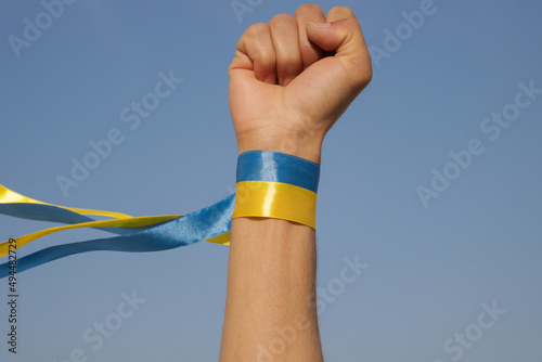 Solidarity with Ukraine. Raised hand with blue and yellow ribbon in support of Ukraine. Concept of resistance. Fist in air with copy space.