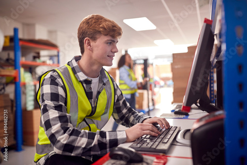 Male Intern Working In Busy Modern Warehouse On Computer Terminal photo
