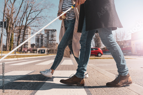 A blind male person using a white cane and walks with his female friend.They walk down the street,laughing and talking.