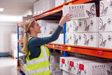 Female Worker Inside Busy Warehouse Putting Box Onto Shelf