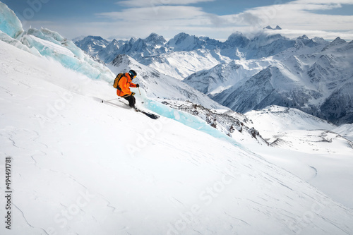A skier is skiing downhill on a sunny day in high mountains. Downhill freeride next to a glacier high in the mountains