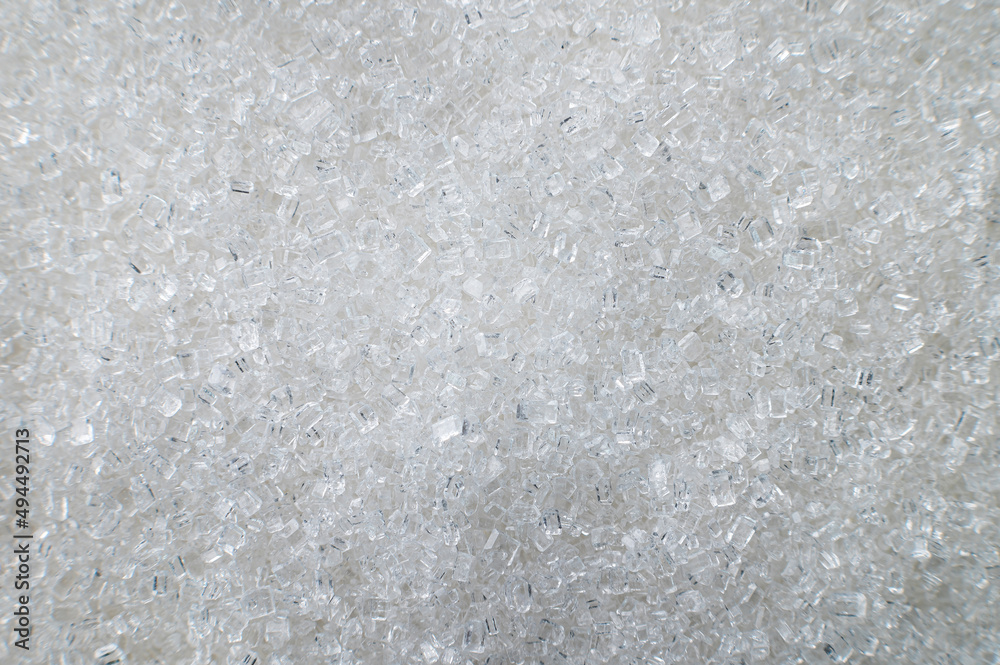 Fototapeta premium Macro shot of white sugar closeup on the surface as an abstract background. Food industry benefits and harms of granulated sugar