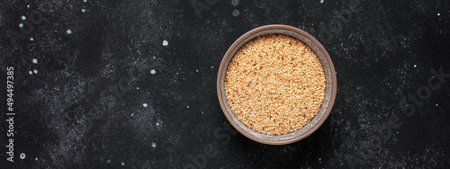 Roasted sesame seeds in a bowl on a black stone background. Top view, banner.