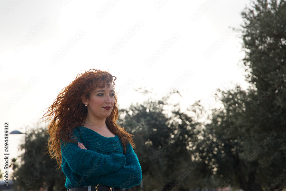 Young woman with red hair, freckles, arms crossed and serious gesture in an outdoor park. Concept loneliness, seriousness, sorrow, worry. Young woman with red hair, freckles, arms crossed and serious gesture in an outdoor park. Concept loneliness, seriousness, sorrow, worry.