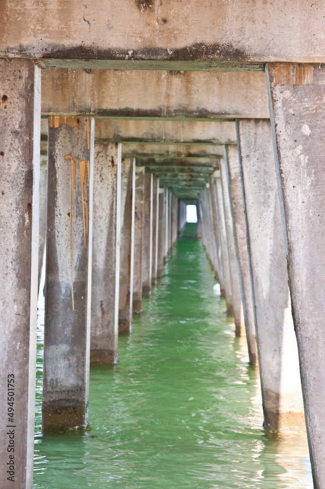 front view, medium distance of a series of concert legs sunk into tropical shoreline, sand, supporting a wood pier in gulf of Mexico front view, medium distance of a series of concert legs sunk into tropical shoreline, sand, supporting a wood pier in gulf of Mexico