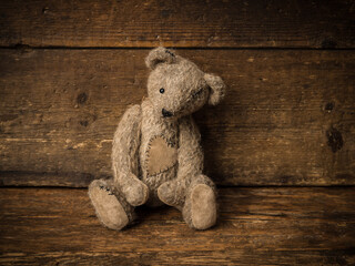 Gray old teddy bear on rustic shelf
