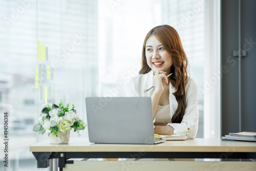 Canvas Print Portrait of Asian young businesswoman with laptop writes on a document at her office,Asian girl working at a office space with a laptop computer