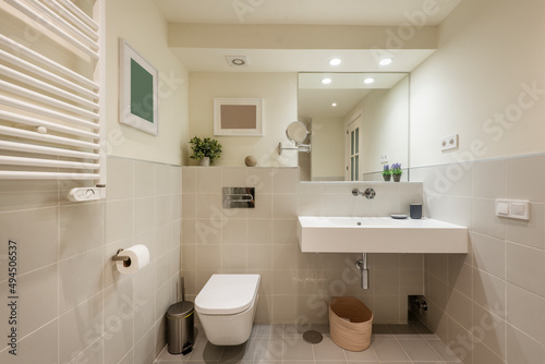 Bathroom with one piece sink, square framed mirror, decorative objects, radiator to dry towels and light colored tiles