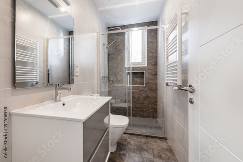 Bathroom with white wooden furniture, frameless mirror, aluminum towel radiator and gray ceramic stoneware floor