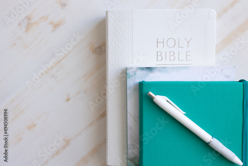 White Christian bible with teal journal and white pen and devotional on a white wood background with copy space