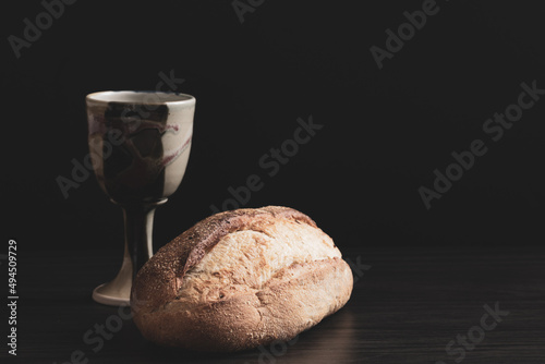 Loaf of bread and clay chalice on a black background with copy space photo