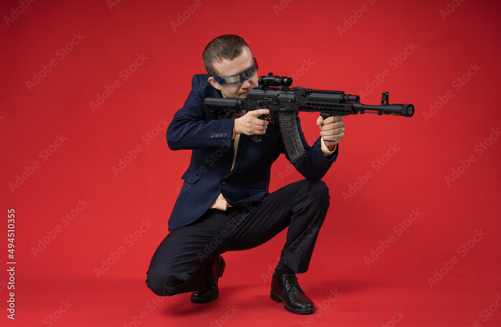 businessman with a gun. a guy in fashionable glasses, a suit holds a machine gun. Business concept. red background businessman with a gun. a guy in fashionable glasses, a suit holds a machine gun. Business concept. red background