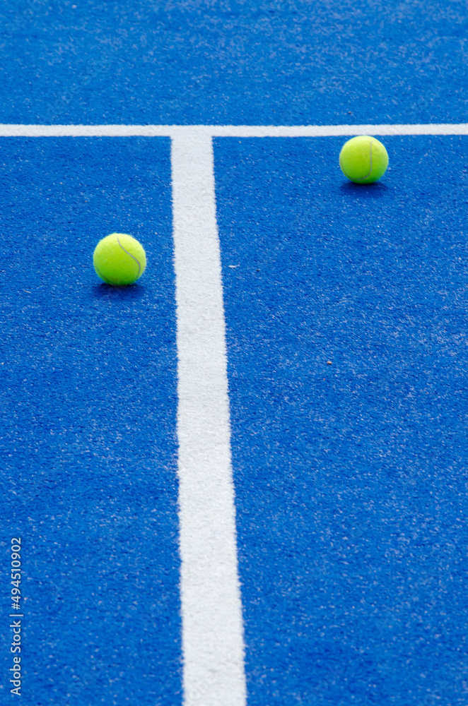 two balls and lines of a blue paddle tennis court