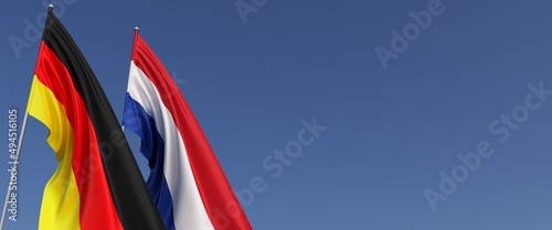 Flags of Germany and Netherlands on flagpoles on the side. Flags on a blue background. Place for text. Berlin, Munich. Holland, Amsterdam. Commonwealth. 3D illustration.