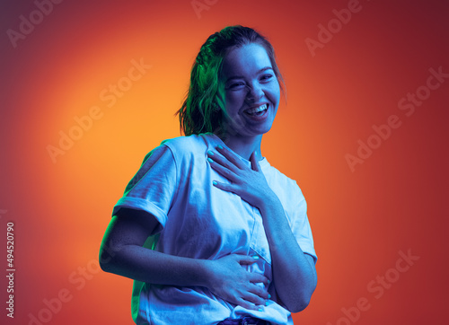 Portrait of young beautiful girl cheerfully laughing and posing isolated over gradient red background in neon light
