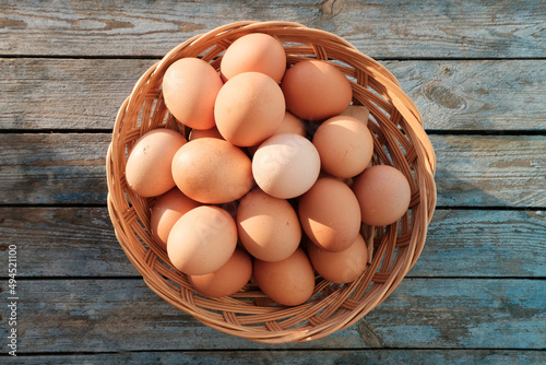 Eggs in a basket under natural sunlight. Dietary farm product. Wooden background.