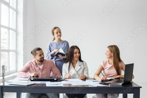 Man and three women work together in office using computers, notepads, graphs and charts.