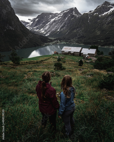 Back view of two girls standing in the grass field and looking at views of Segestad Norway Stryn photo