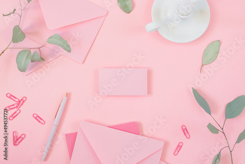 Blank business card mock up in the centre of composition made of white ceramic candle holder, notepad, envelopes, paper clips, pen in pastel shades of pink.