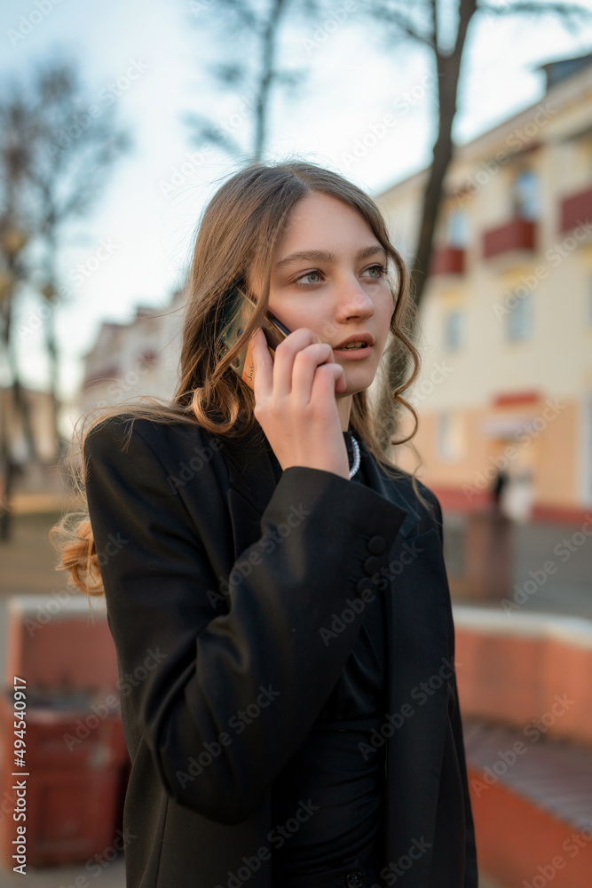 Portrait of a young beautiful girl in a business suit talking on the phone on a city street.