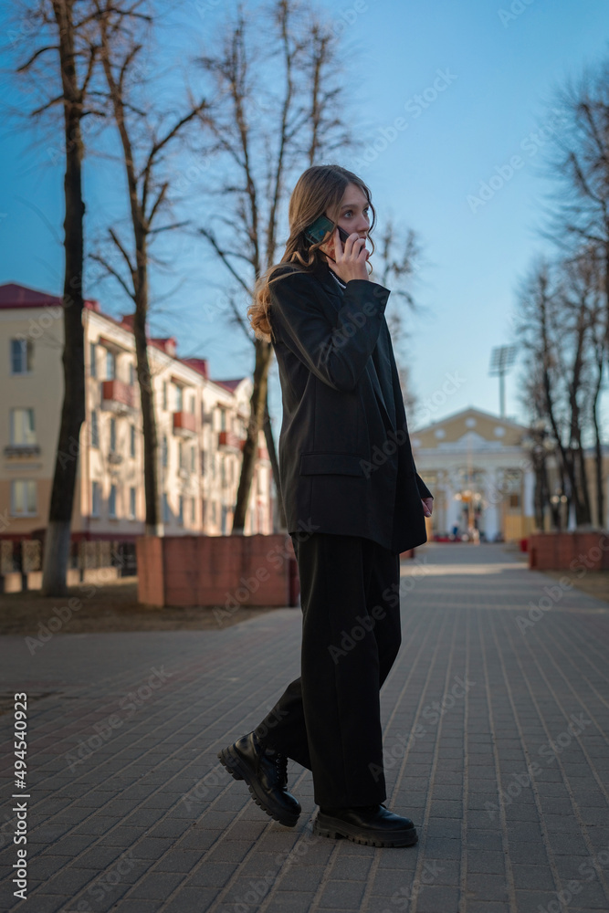 Portrait of a young beautiful girl in a business suit talking on the phone on a city street. Portrait of a young beautiful girl in a business suit talking on the phone on a city street.