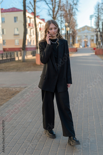Portrait of a young beautiful girl in a business suit talking on the phone on a city street.