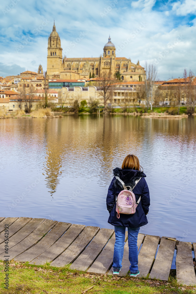 Fototapeta premium Woman next to the Tormes river, observing the gothic cathedral that is reflected in the water.