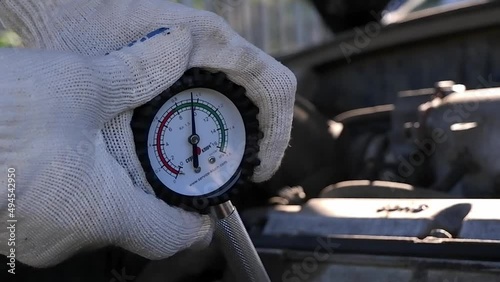 Measurement of compression in a car engine.A white man's gloved hand holds a compressor meter against the background of a car engine. The pressure gauge shows the operating pressure.