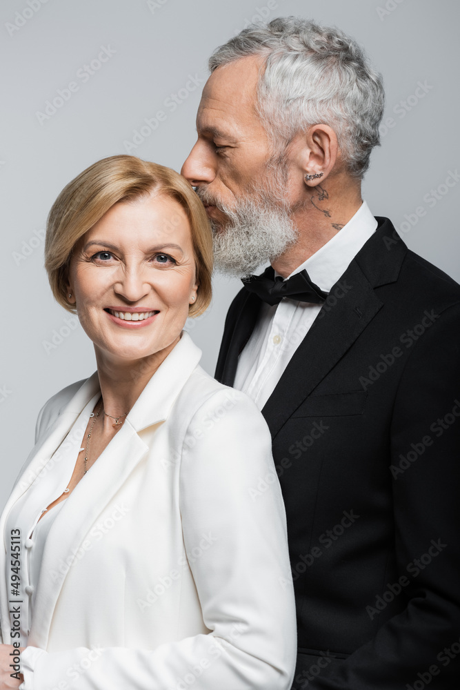 Portrait of mature groom kissing head of smiling bride isolated on grey. Portrait of mature groom kissing head of smiling bride isolated on grey.