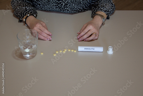 A woman's hands resting on the table with a glass of water and anxiolytic pills.  photo