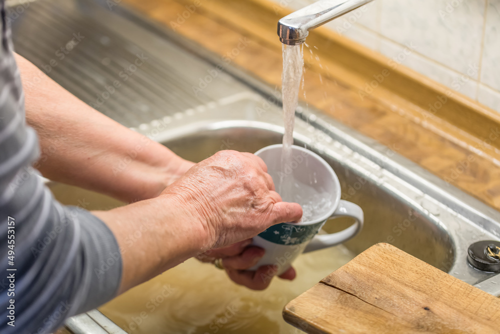 Alte Frau Oma beim Abspülen von Geschirr Kaffeetasse Tasse in einer Spüle mit laufendem Wasser aus Wasserhahn in einer Küche, Deutschland Alte Frau Oma beim Abspülen von Geschirr Kaffeetasse Tasse in einer Spüle mit laufendem Wasser aus Wasserhahn in einer Küche, Deutschland
