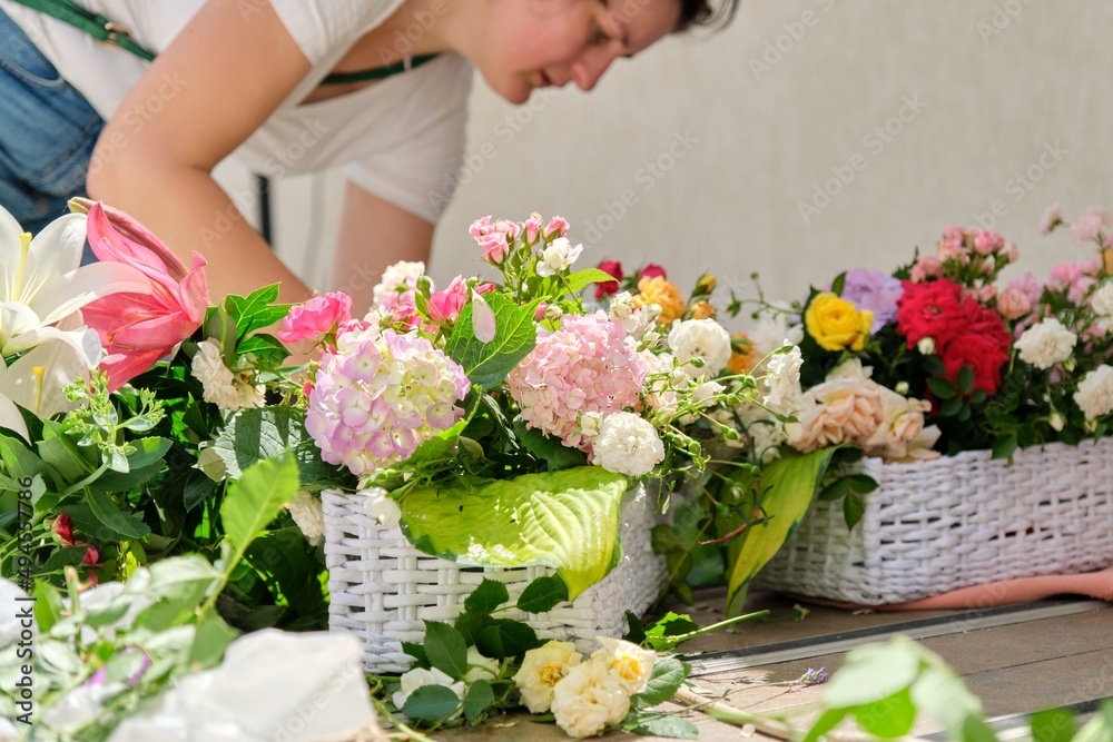 Woman florist making flower arrangement in basket outdoor.
