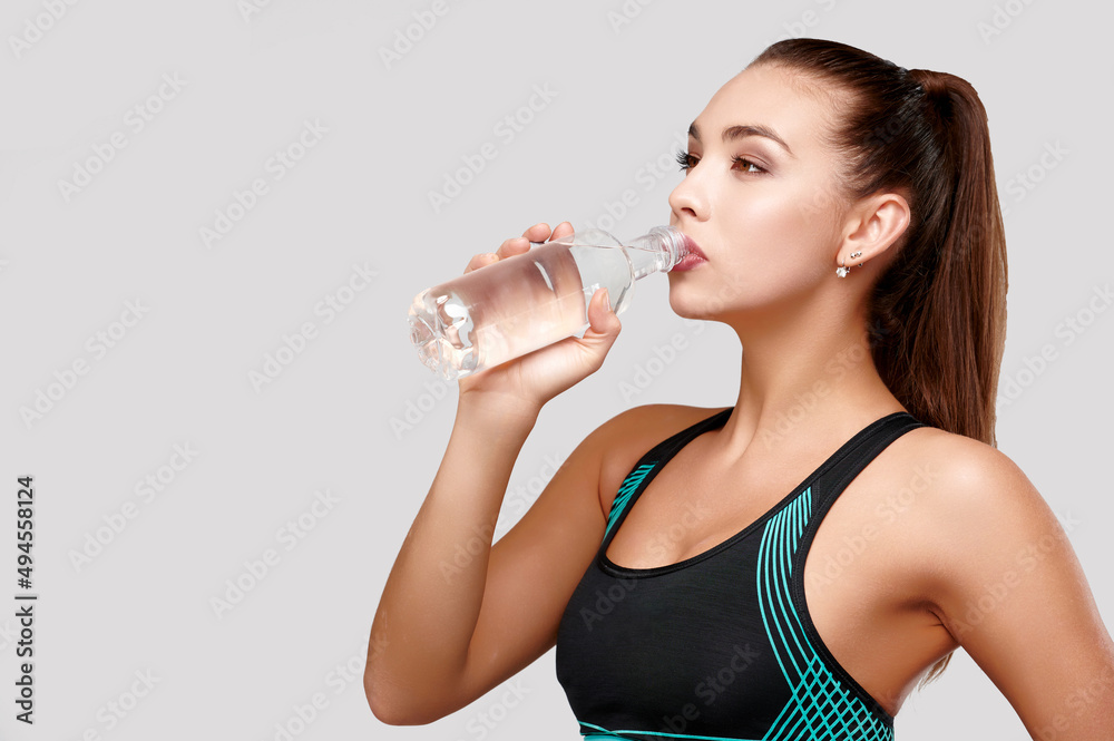 Strong sporty caucasian woman in black fitness suit drinks water on isolated gray background Strong sporty caucasian woman in black fitness suit drinks water on isolated gray background