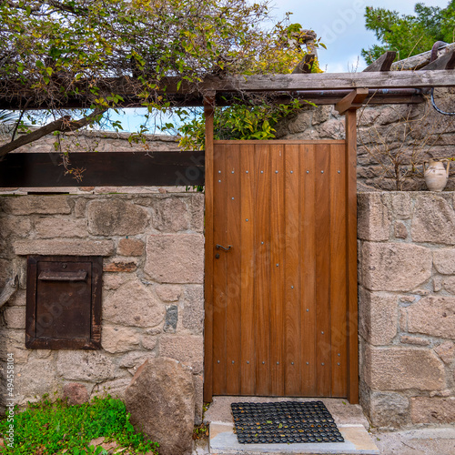 A wooden door with a stone fence, pergola and foliage by the street, Pachia Rahi village, Aegina island, Greece photo