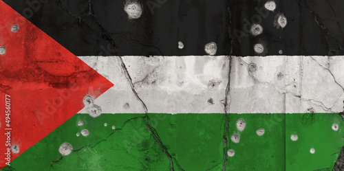 Full frame photo of a weathered flag of Palestine painted on a cracked wall with bullet holes. Violence and war in Palestine concept.