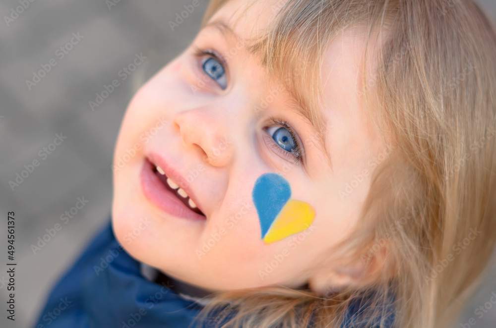 portrait of a girl with a blue and yellow heart on the cheek  - obrazy, fototapety, plakaty 