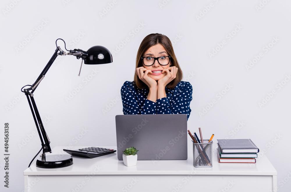 Photo of nervous worried office employee lady sit desk bite fingers wear dotted blouse isolated grey color background Photo of nervous worried office employee lady sit desk bite fingers wear dotted blouse isolated grey color background