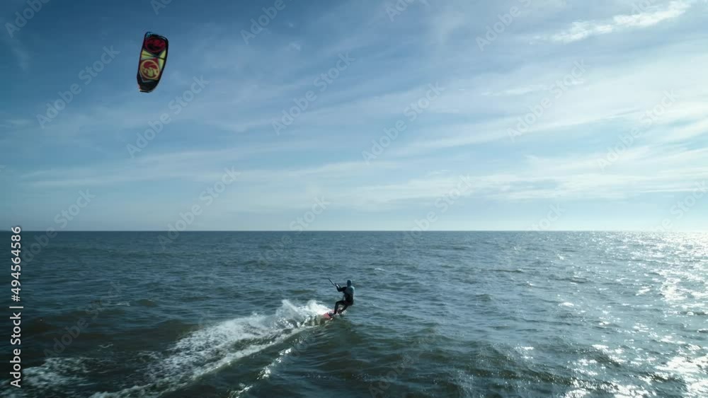 In this aerial drone camera shot you can see fearless extreme sport lover – kiteboarder riding ocean water with his kite flying in the blue sky.