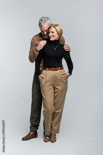 Stylish bearded man hugging blonde wife in turtleneck on grey background.