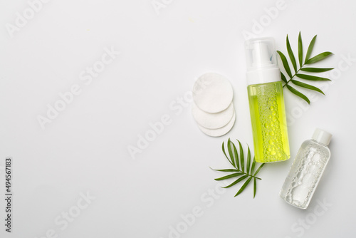 Foaming facial cleanser and micellar water on color background, top view