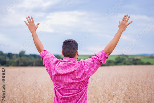 Amazing view with man standing with his back to the camera with open arms thanking for the wheat harvest. The farmer checks the natural organic crop