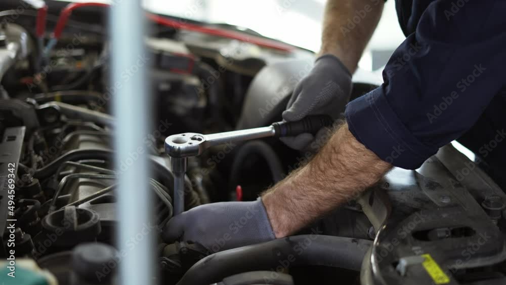 Car mechanic using wrench to repair the engine in a car service, close up