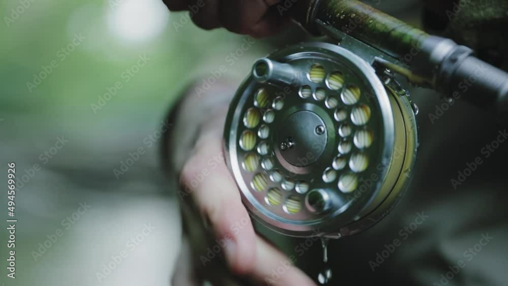 Fisherman is holding rod and line spool in hands. Water drops slowly dripping down and starts splashing when fishing reel starts to spin.