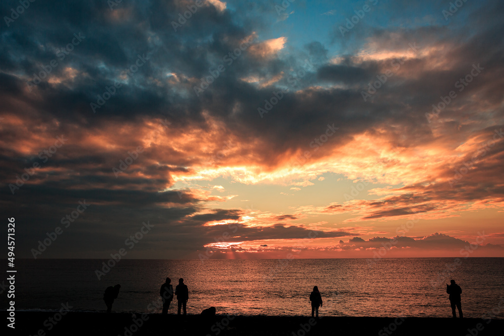 Mediterranean coast at sunset, in Turkey, Antalya, silhouettes of people, orange sky.
