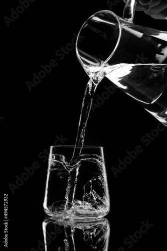 water pours into a glass from a decanter on black background