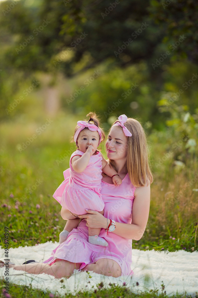 Obraz premium mother and daughter in pink dresses sit on a white blanket
