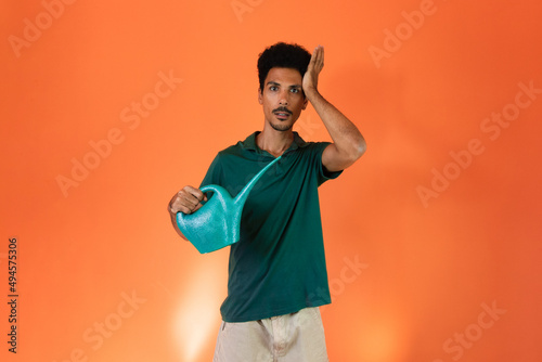 Earth Day - Handsome young black man with green watering can holding plant isolated on orange background.