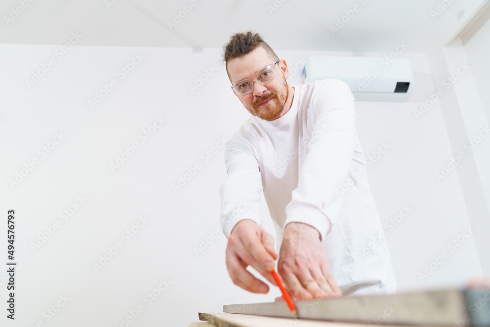 carpenter in protective glasses makes measurements and draws on wood