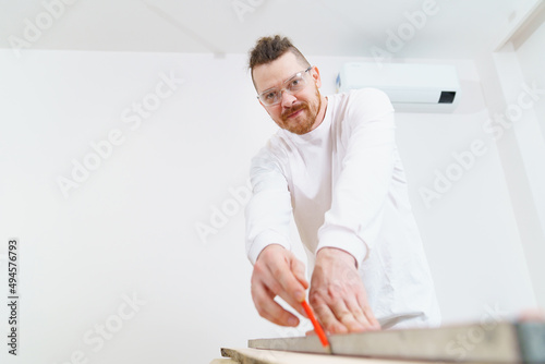 carpenter in protective glasses makes measurements and draws on wood © andrey
