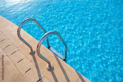 Fotografia Close up of swimming pool stainless steel handrail descending into tortoise clear pool water